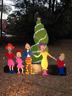 a group of people standing next to a christmas tree on top of a wooden stump