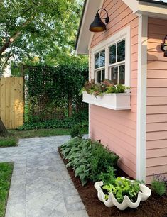 a small pink house with plants growing in the window boxes and on the outside wall