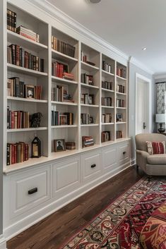 a living room filled with lots of white bookshelves next to a large rug