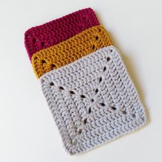 three crocheted squares with holes in them on a white surface, one is yellow and the other is red