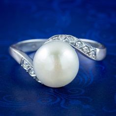 An elegant vintage crossover solitaire ring crowned with a large, cultured pearl with a bright, creamy tone and exceptional lustre. It's set on an 18ct white gold band that twists gracefully around it, with milgrain and twinkling diamonds chasing down each shoulder.   Pearls are the birthstone of June and a true treasure of the ocean, produced organically by fresh and saltwater molluscs. Their spherical shape and exceptional lustre have long been associated with the beauty of the moon and are sy Natural Pearl Ring, Pearl And Diamond Ring, Vintage Pearl, Diamond Brooch, Twist Ring, White Gold Band, Vintage Pearls, Pearl Diamond, Gold Band