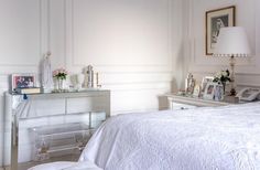 a bedroom with white walls and furniture in the corner, along with a mirrored chest of drawers