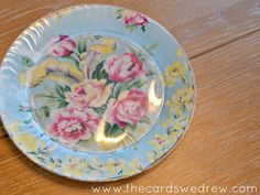 a plate with flowers painted on it sitting on a wooden table next to a lit candle