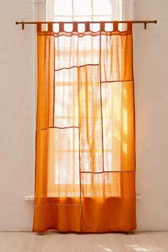 an orange sheer curtain hanging from a window sill in front of a white wall