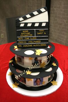 a three tiered cake decorated with film reels and stars on the top, sitting on a red table cloth