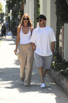 a man and woman walking down the street together, both in white shirts and khaki pants