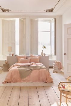 a bedroom with white walls and wooden flooring has a pink comforter on the bed