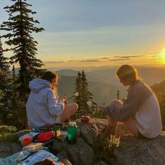 two people sitting on top of a mountain at sunset