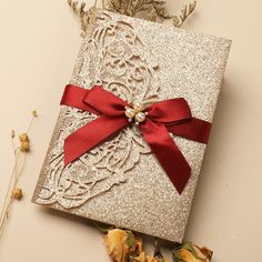 a box with a red ribbon on it next to some dried flowers and leaves,