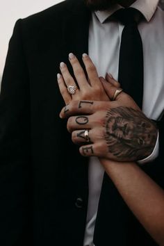 a man in a suit and tie holding his hands together with tattoos on their arms