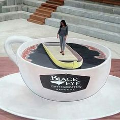 a woman standing on top of a coffee cup with a surfboard in the middle