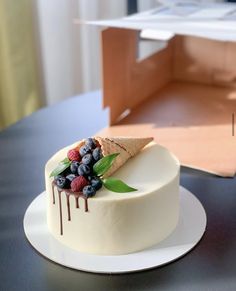 a white cake with berries and ice cream on top sitting on a table next to an open box