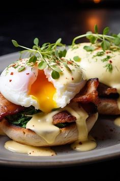 two eggs are on top of an english muffin with cream sauce and sprouts