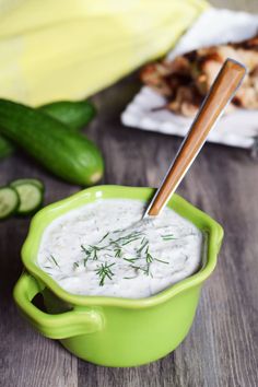 a green bowl filled with white sauce next to cucumbers