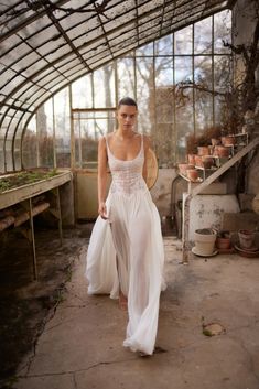 a woman in a white dress walking through a greenhouse