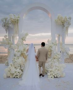 a bride and groom walking down the aisle to their wedding ceremony on the beach at sunset