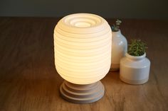 a white lamp sitting on top of a wooden table next to a vase and potted plant