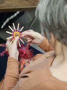 an older woman is working on something with yarn and wood dows in front of her