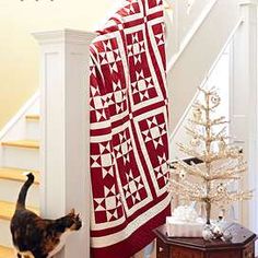 a cat standing next to a red and white quilt on a stair case near a christmas tree