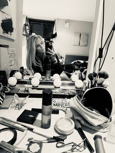 a black and white photo of a woman looking at her reflection in a mirror with makeup products on the table