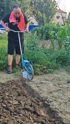 a man using a shovel to dig dirt in the ground with a blue wheelbarrow