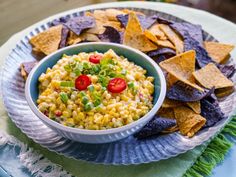 a bowl of corn salad and chips on a blue plate with green napkin next to it