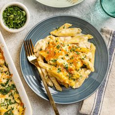 a blue plate topped with pasta covered in cheese and spinach next to a bowl of pesto