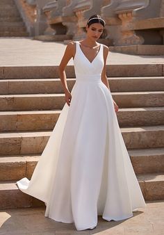 a woman in a white wedding dress standing on some steps with her hand on her hip