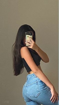 a woman taking a selfie with her cell phone in front of her face and wearing high waist jeans