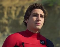 a close up of a person wearing a red shirt and holding a surfboard in his hand