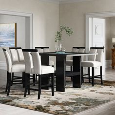 a dining room table with white chairs and a rug on the floor in front of it