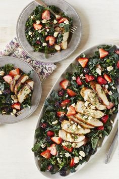 two plates filled with chicken, strawberries and greens