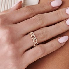 a woman's hand with a gold ring on her left wrist and pink manicured nails