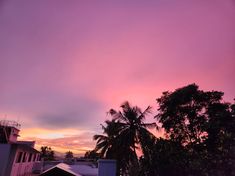 the sky is pink and purple as the sun sets over some buildings with palm trees