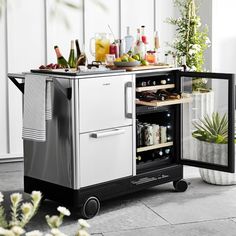 an open refrigerator with drinks on it in a room next to plants and flowers,