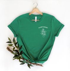 "Plant Daddy Pocket Tee, Plant Dad Shirt, Plant Lover Shirt, Houseplant Shirt, Plant Shirts For Men, Plant Lovers Gift, Plant Daddy T-Shirt Please Check All Photos For Details.   🐞Choose Your T-Shirt Size From The Drop-Down Lists Next To The item Picture   ⭐Choose Of Your T-Shirt Color From The 2nd Picture   🐞Use \"Add message to Seller\" link On The Checkout Page To Send me the Following important Details For Your Order's Customization.   ⭐Shipping Time Varies by location (we are located in Sugar Land, Texas) please consider that our turn around time is 1 to 3 business days.     ⭐Which brand do you use for t-shirts? We use Gildan Softstyle, Bella Canvas Unisex, Hanes, Outlash, Tees,  District and Next Level when we have a shortage of stocks for certain colors and sizes. Our printing met Green Graphic Tee With Plant Print, Green Short Sleeve Tops With Plant Print, Green Graphic Tee With Plants Print, Green Short Sleeve Shirt With Plant Print, Green Tops With Plant Print Short Sleeves, Green Graphic Tee With Text Print, Green Graphic Tee Shirt With Text Print, Relaxed Fit Green T-shirt With Plant Print, Green Cotton Top With Text Print