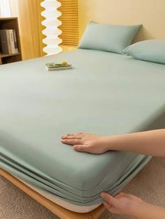 a person reaching for the bottom of a bed that is made up with blue sheets