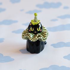 a small black cat figurine wearing a party hat and striped shirt with polka dots