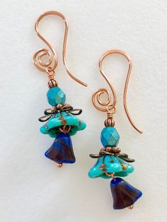 "Adorable new Czech glass Premium flower earrings in turquoise and lapis blue with aqua luster beads and copper accents. Opaque blue turquoise wide bellflowers with copper Picasso finish are accented with little Czech glass lilies in lapis blue opaline with metallic wash and aqua blue luster beads. Wire wrapped in bright copper with copper accents. Ear wires are handmade in German copper with cute spiral design. Total drop is 2\"." Turquoise Czech Glass Flower Earrings For Gift, Blue Czech Glass Wire Wrapped Beaded Earrings, Picasso Flowers, Blue Czech Glass Flower Jewelry, Blue Czech Glass Flower Earrings, Vintage Turquoise Czech Glass Earrings, Glass Flower Earrings, Blue Flower Earrings, Bright Copper