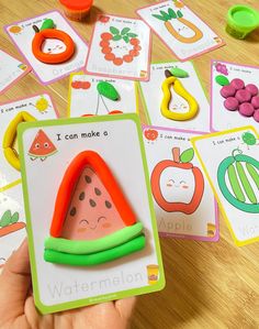 a child's hand is holding a card game with fruits and vegetables on it