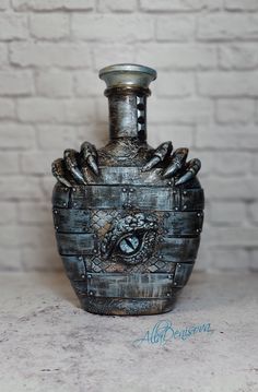 a metal vase sitting on top of a counter next to a brick wall with an eye in it