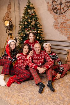 a family in matching christmas pajamas sitting next to a christmas tree