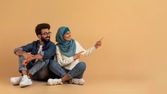 a man and woman sitting on the floor pointing at something in front of their faces