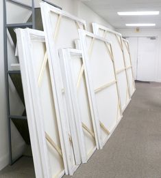 a row of white frames sitting on top of a floor next to a book shelf