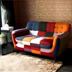 a multicolored couch sitting in front of a brick wall next to a window