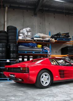 a red sports car parked in a garage next to shelves with tires and other items