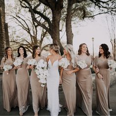 a group of women standing next to each other in front of trees and holding bouquets