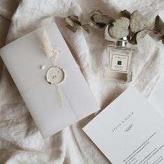 wedding stationery items laid out on a bed with white linens and dried flowers