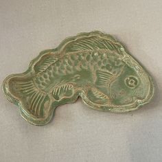 a green fish shaped dish sitting on top of a white tablecloth covered floor next to a wall