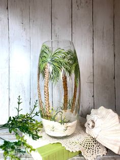 a glass vase with palm trees in it sitting on a table next to a book